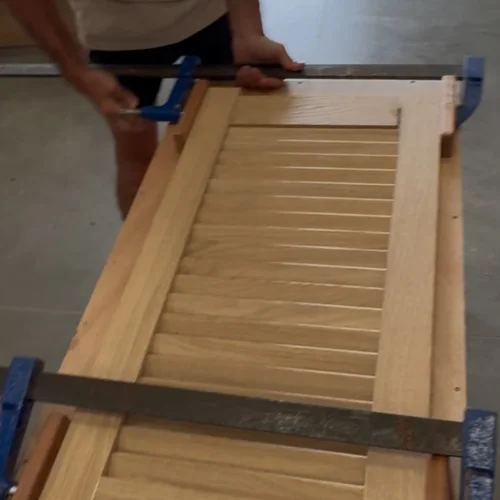 Porte persienne en bois massif terminée, serrée aux serre-joints